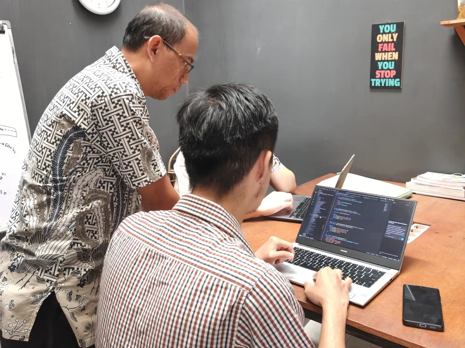 Pembimbing membungkuk memeriksa kode program di laptop peserta
