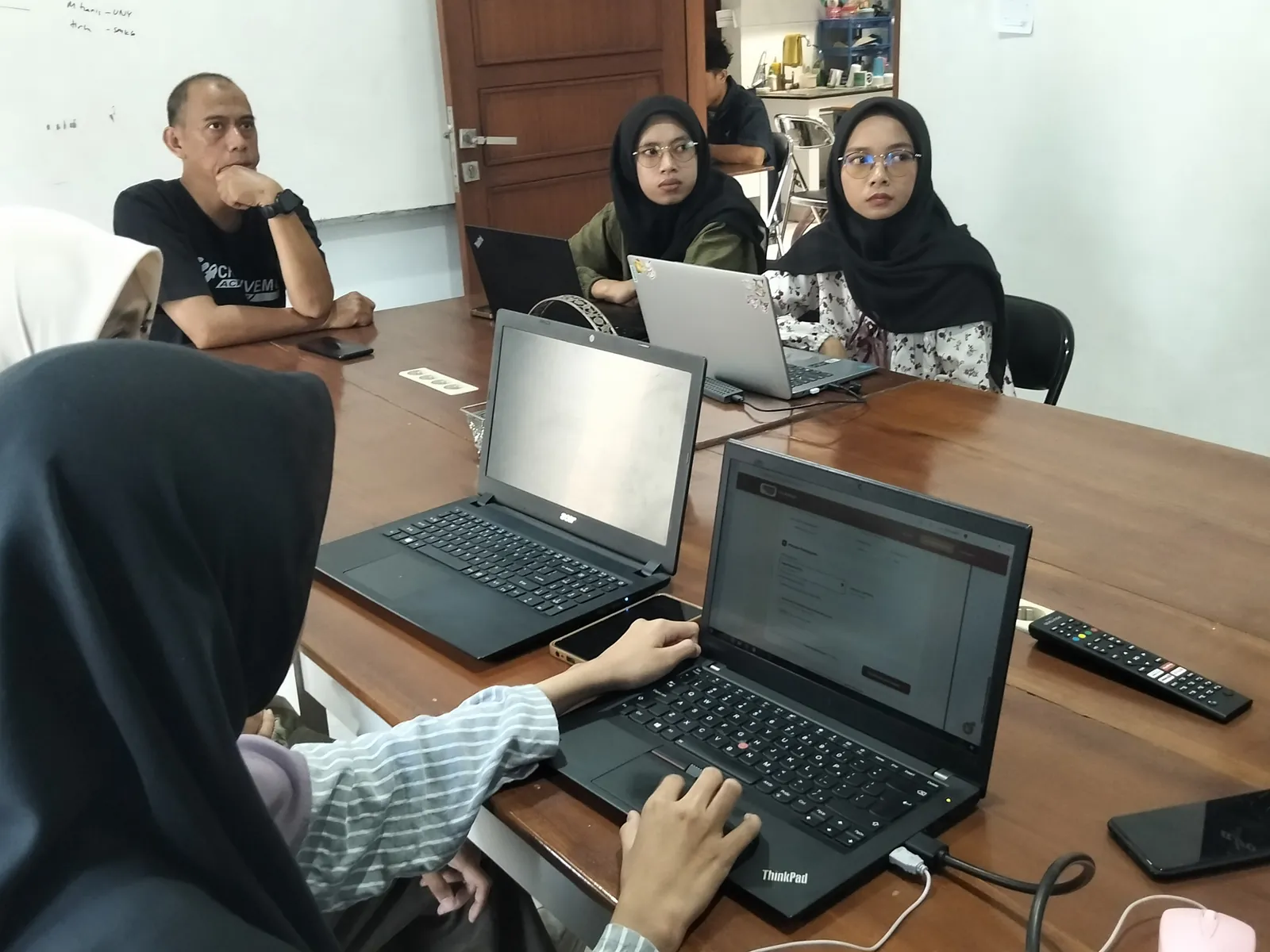 Peserta bekerja dengan laptop sementara pembimbing berdiskusi di ujung meja