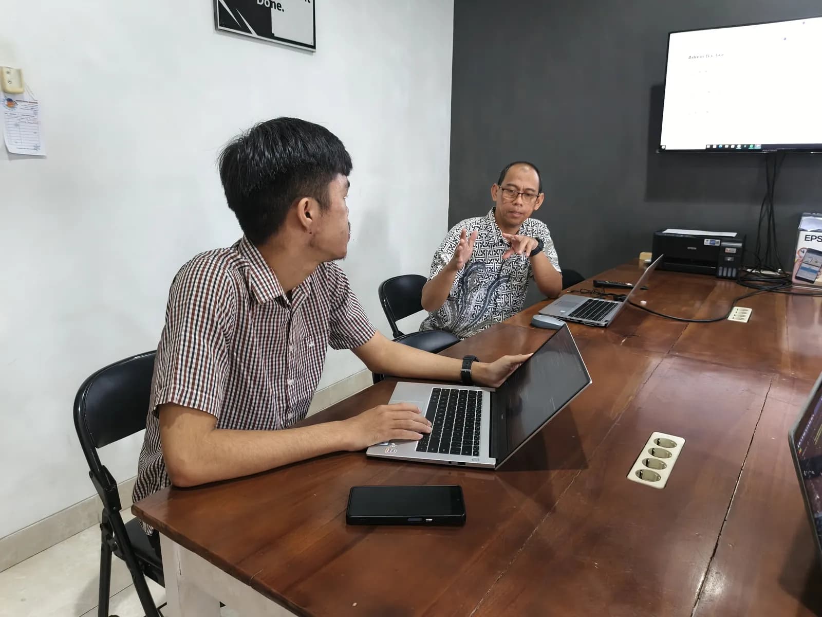 Peserta berbicara dengan pembimbing di meja kerja sambil membuka laptop