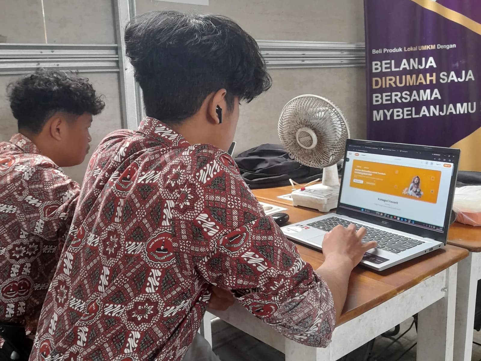 Dua siswa SMK berseragam batik bekerja dengan laptop